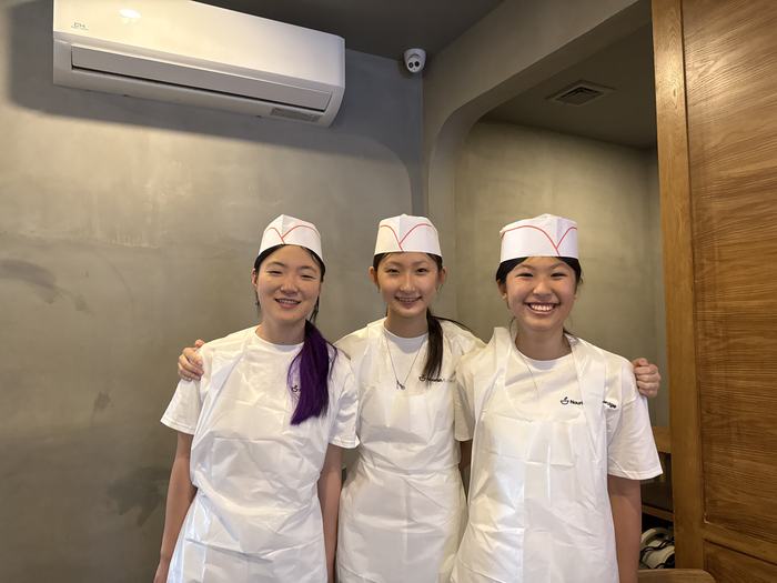 Three volunteers in paper chef hats and aprons after a kitchen shift.