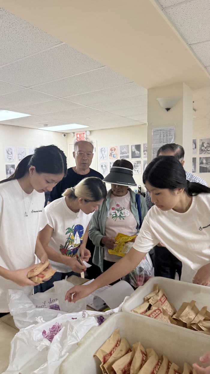 Volunteers and neighbours sorting wrapped meals and bags at a long table.
